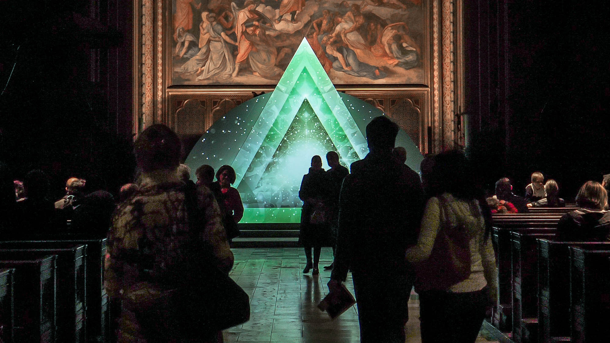 Image of a video art installation in a church with people. Triangle with geometric and ornamental design. Light art show in a church