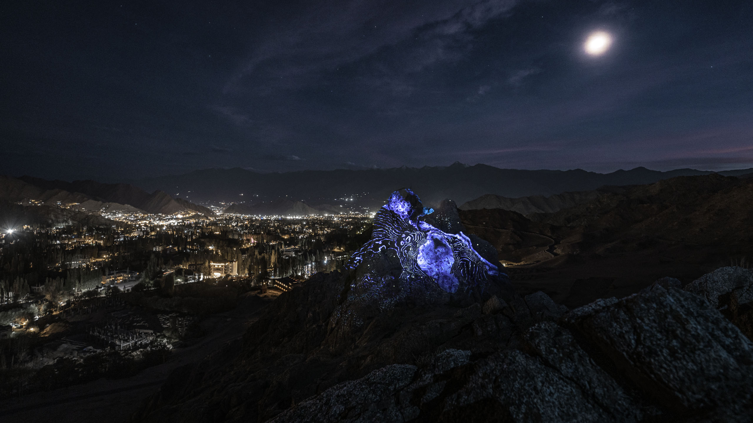 Land art projection mapping artwork on a rock with blue visuals  in a nightly mountain scenery