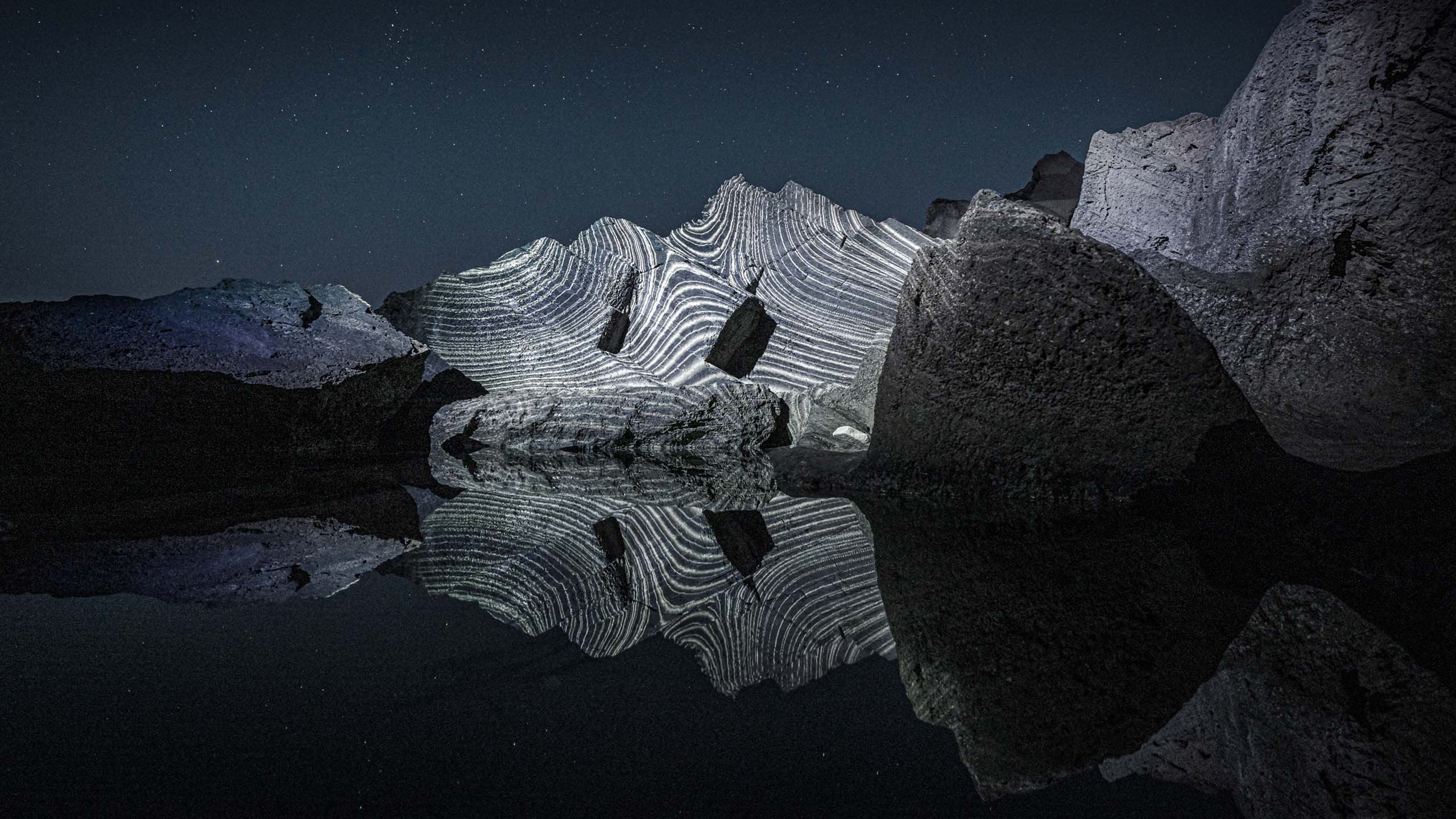 Land light art video projection installation in nature on a group of rocks with reflections in the water, Formentera