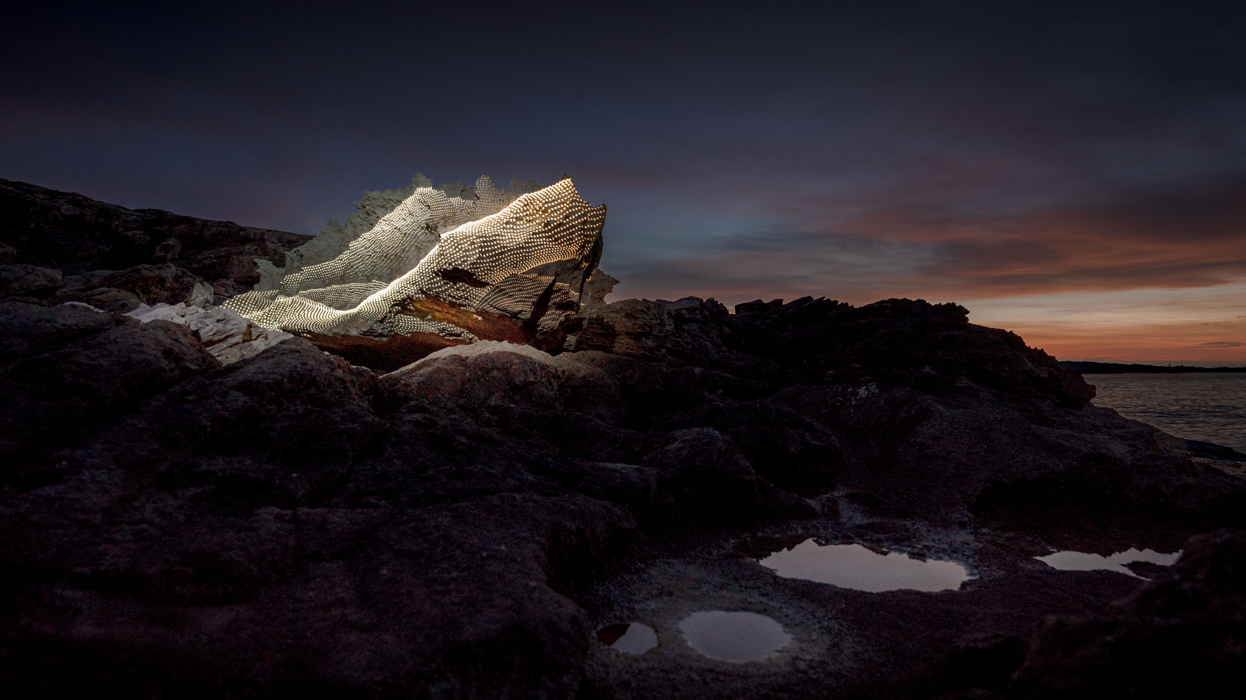 Light art videomapping projections on a beautiful boulder in a surreal landscape ion the sea coast