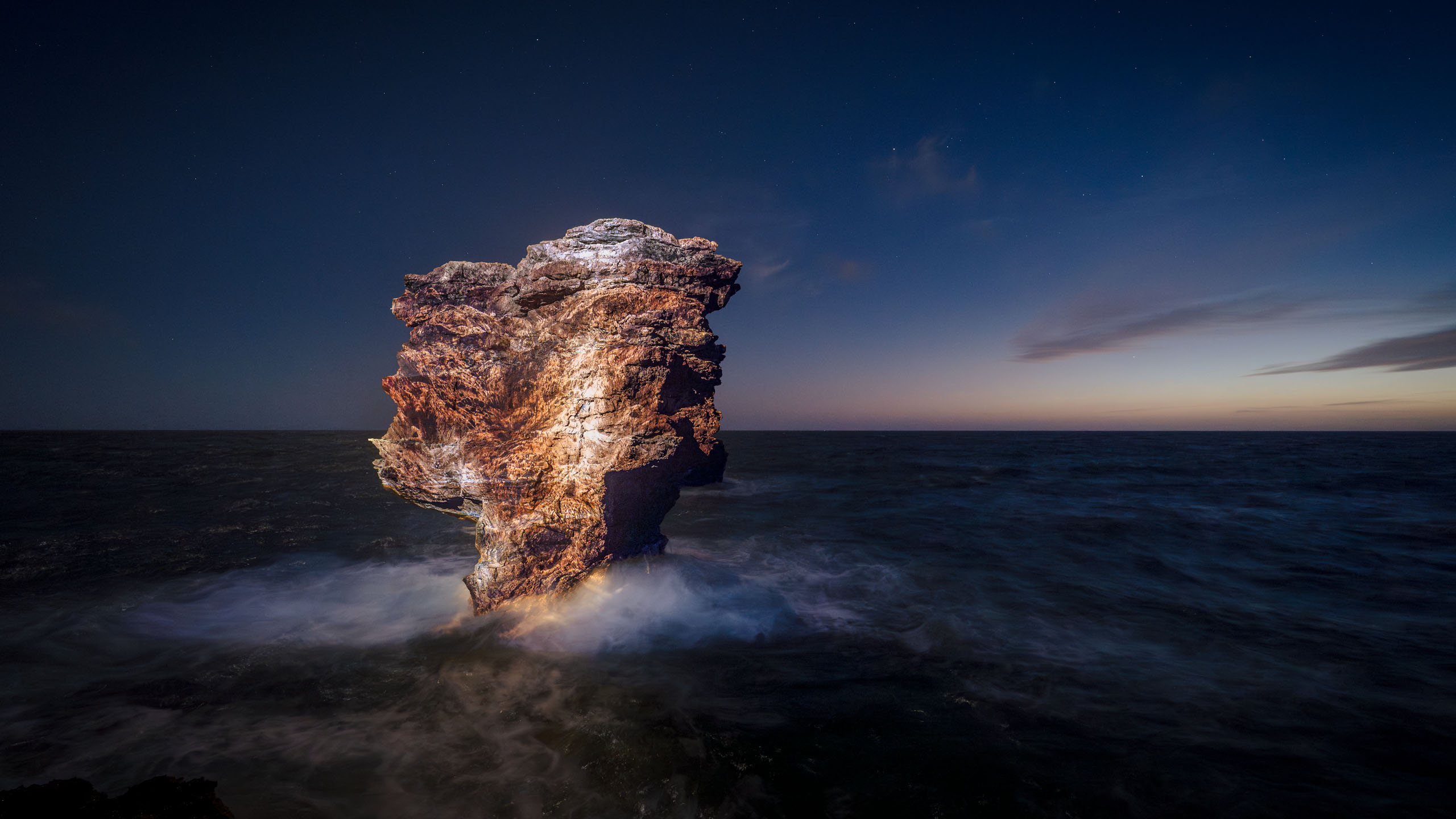 Photo art videomapping light installation on a beautiful boulder in  the sea at night 