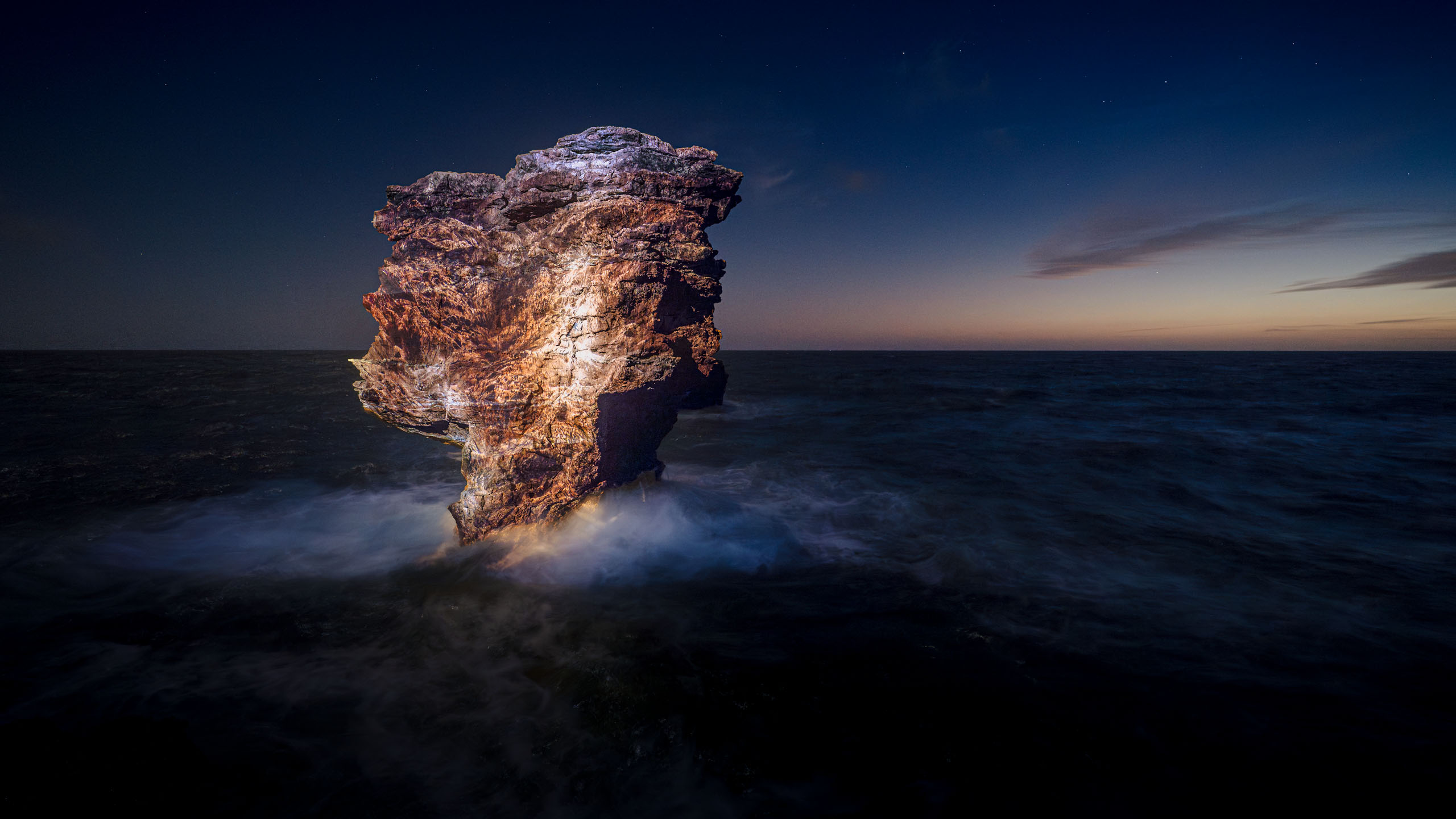 Photo art videomapping light installation on a beautiful boulder in  the sea at night 