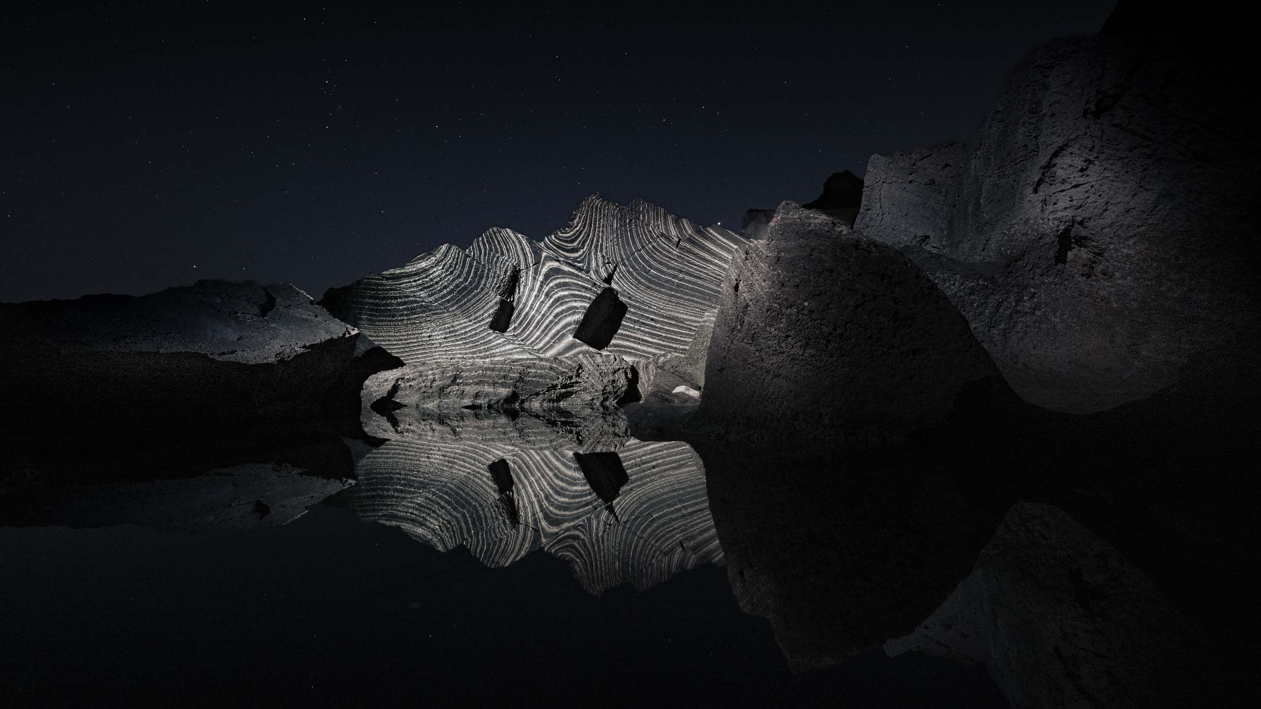 Land light art video projection installation in nature on a group of rocks with reflections in the water, Formentera