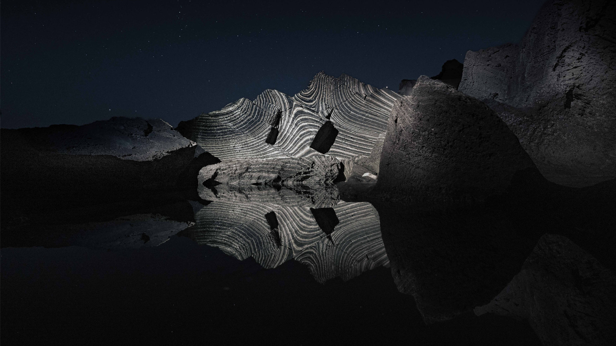 Land light art video projection installation in nature on a group of rocks with reflections in the water, Formentera
