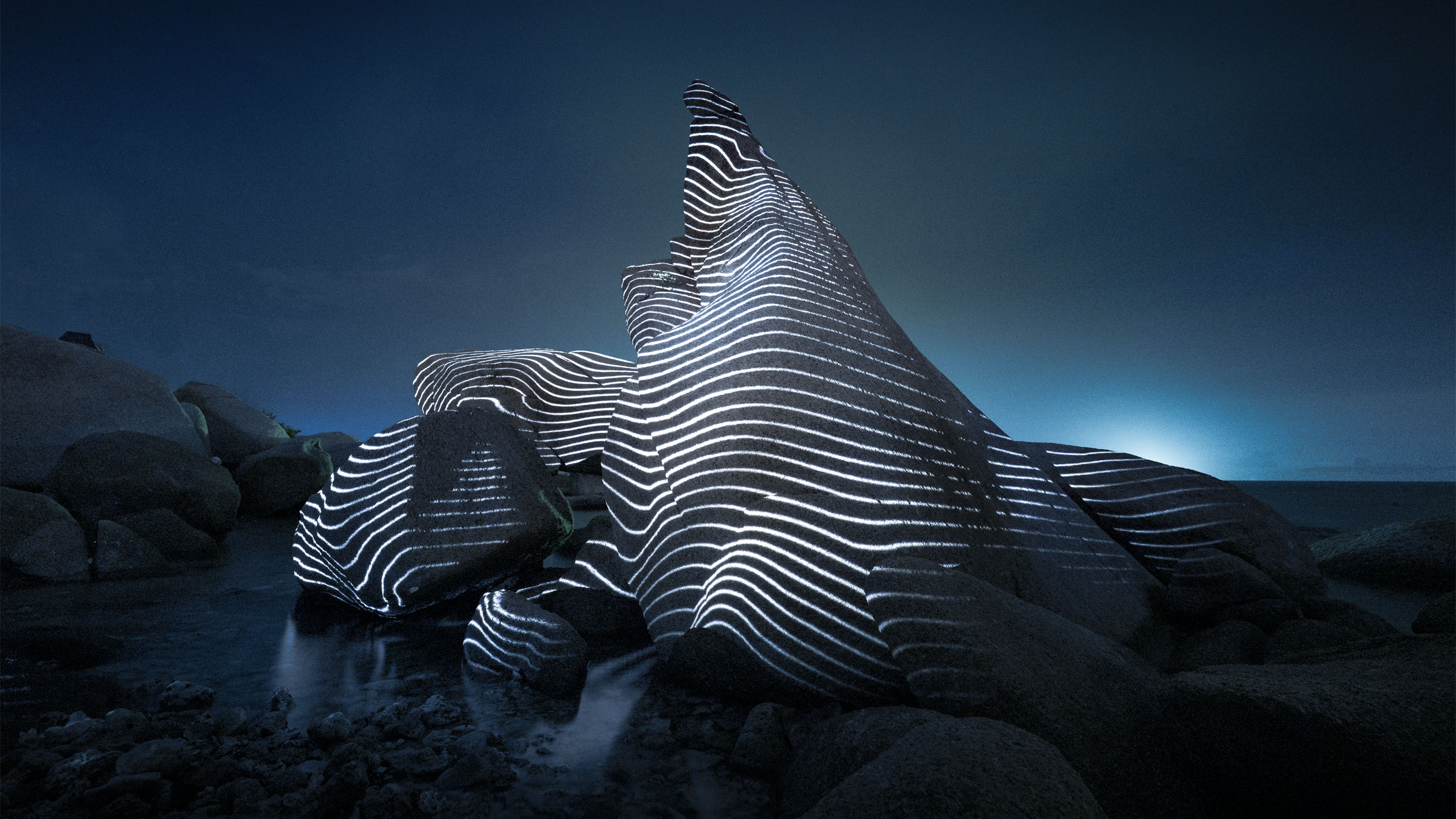 Projection mapping artwork on coastal rock formation in Thailand, featuring luminous topographic contour lines across stone at night.