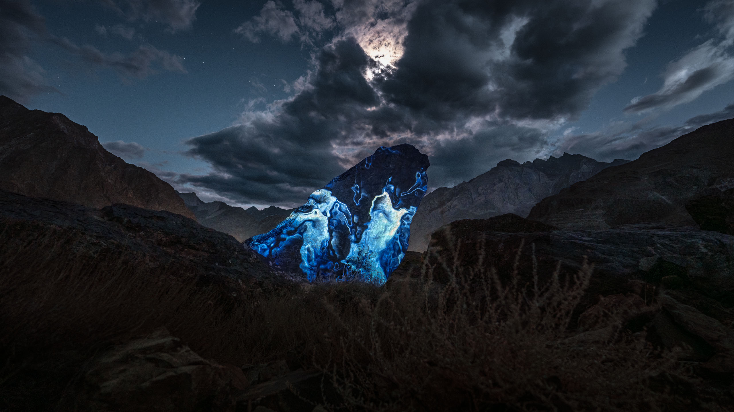 CHU – Liquid States | Audiovisual Rock Projection, Ladakh Blue audiovisual light projection on Himalayan rock under dramatic night sky, part of CHU – Liquid States by Philipp Frank.